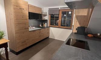A modern kitchen with wooden cabinets and an elegant countertop. Large windows provide plenty of light.