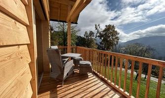 A cozy wooden porch with two chairs and a table. In the background, there is a beautiful view of the mountains and the sky.