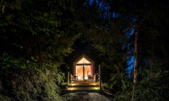 A cozy wooden house in the forest at night. Light radiates from the windows, creating an inviting atmosphere.
