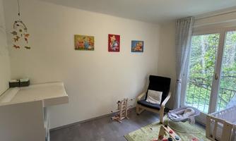 A bright children's room with a chair, a rug, and colorful pictures on the wall. The windows let in plenty of daylight and offer a view of the greenery.