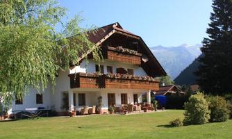 A beautiful chalet with a balcony and flowers, surrounded by green meadows. The mountains can be seen in the background.