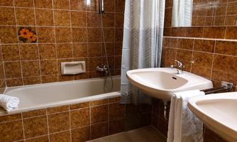 A bathroom with a brown tiled pattern, a bathtub, and a sink. A white curtain and towels complete the picture.