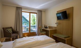 A bright and cozy hotel room with a double bed, a desk, and a comfortable armchair. Large windows provide a view of a green landscape.