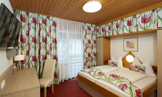 A cozy bedroom with a large bed and colorful curtains. A television and a wooden table complement the furnishings.