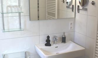 A modern bathroom with a white sink and mirror. Next to the sink are towels and a small stool.
