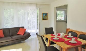 A bright living room with a comfortable sofa and a dining table. On the table are coffee mugs and red placemats.