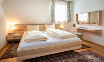 A cozy bedroom with a double bed and wooden furniture. Plenty of light shines through the window, creating an inviting atmosphere.
