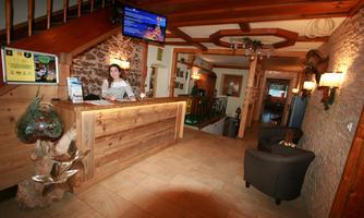 An inviting reception hall with wooden decor and cozy furniture. In the background, a television is visible, and a staff member is welcoming the guests.