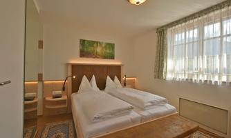 A cozy bedroom with two single beds and a wooden chair. Large windows provide plenty of daylight and a pleasant atmosphere.