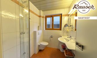A modern bathroom with a shower, sink, and toilet. Bright tiles and a large window create a friendly atmosphere.