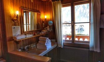 A cozy bathroom with wooden walls and a large window. Fresh towels are on the washing machine, and a mirror stands in the corner.