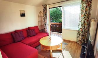 A cozy living room with a red sofa and a round coffee table. Large windows provide plenty of daylight and offer a view outside.