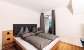 A modernly furnished bedroom with a double bed and beautiful pillows. Large windows and cozy wooden floors create an inviting atmosphere.