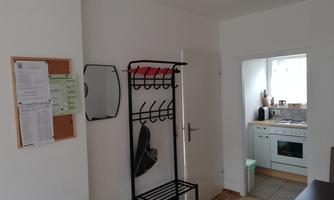 A simple room with a coat rack and a small kitchen. The space is bright and functionally designed.