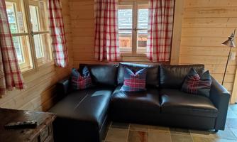 A cozy seating area with a black couch and checkered cushions. The room has wood paneling and large windows with red curtains.