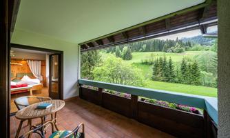 A cozy balcony overlooking green meadows and trees. In the background, gentle hills can be seen.