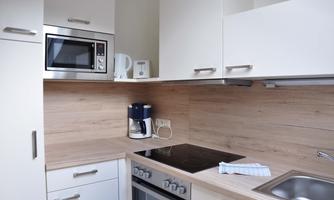 A modern kitchen with white cabinets and wooden paneling. It is equipped with a microwave, a coffee machine, and a ceramic cooktop.
