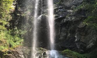 A beautiful waterfall cascading over rocky steps, surrounded by green foliage. Nature feels peaceful and inviting.