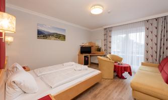 A cozy hotel room with a double bed, a television, and a sitting area. Large windows let in plenty of light and offer a view of nature.