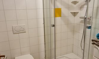 A modern bathroom with a glass shower and a toilet. The floor is designed with black and white tiles.