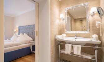 An elegant bathroom with a sink and bright tiles. In the background, there is a bedroom with a comfortable bed.