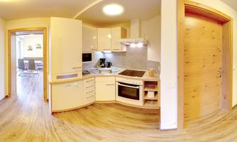 A modern kitchen with bright furniture and wooden flooring. The space is well-lit and has an open design.