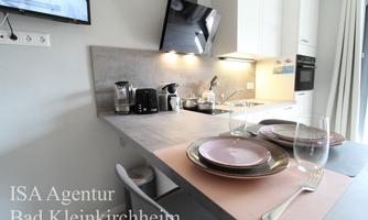 A modern kitchen with a dining area. Dishes and glasses are set on the table, and a television is mounted on the wall.