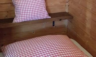 A cozy room with wood paneling. On the bed are large pillows with a red-and-white checkered pattern.