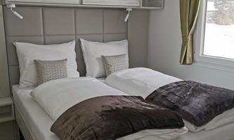 A cozy bedroom with two single beds and soft pillows. The room has large windows and bright, modern furniture.