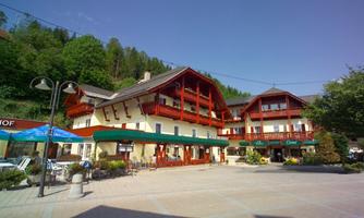 An inviting hotel with a red-and-white balcony and a beautiful terrace. Surrounded by trees in a quiet environment.
