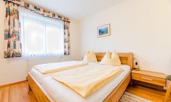 A cozy bedroom with a double bed and light bedcovers. Large windows provide plenty of daylight and a friendly atmosphere.