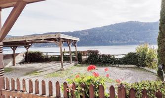 A serene view of a lake with mountains in the background. In the foreground, there is a wooden fence with blooming flowers.