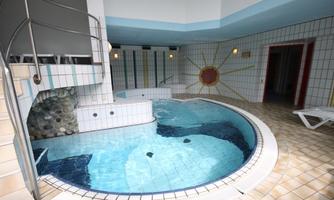 An elegant indoor pool with a round basin and tiles in light colors. The walls are decorated, and there are cozy loungers for relaxation.