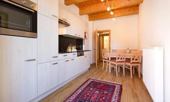 A modern kitchen with light cabinets and wooden ceilings. A dining table with chairs and a rug in the foreground create an inviting atmosphere.