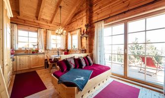 A cozy living space with wooden paneling and large windows. A seating area with red cushions and a view of the terrace.