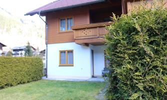 A cozy wooden house with a balcony and a well-maintained garden. In the background, the mountains are visible.