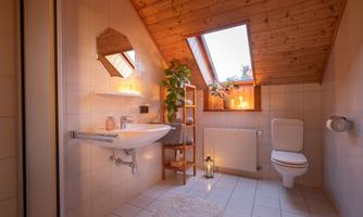 A modern bathroom with a wooden ceiling and natural elements. There is a bathtub, plants, and soft light from candles.