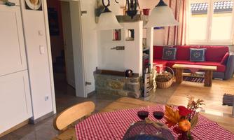 A cozy living kitchen with a round table and beautiful decorations. In the background, there is a red sofa and windows with plenty of light.