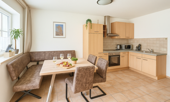 A modern kitchen with a dining area. The table is set with a fruit bowl and drinks.