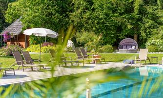 A beautiful pool area with loungers and umbrellas. Surrounded by green plants and trees for a relaxed atmosphere.