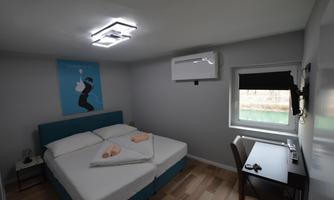 A modern bedroom with a double bed and a desk. An artwork hangs on the wall, and there is a window with a view outside.