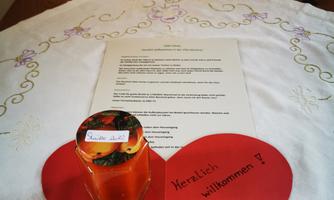 A heart made of red paper with the inscription "Welcome!" is lying on a table. Above it is a glass with an orange liquid and a sheet of paper with information.