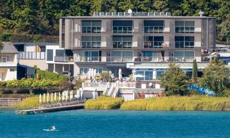 A modern building by the water with a beautiful terrace. In the foreground, someone is paddling on a lake.