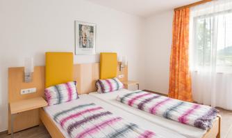 A modern bedroom with two single beds and colorful bed linens. Large windows provide plenty of daylight and a friendly atmosphere.