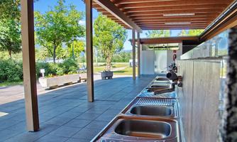 A modern outdoor area with several stainless steel sinks. Surrounded by trees and a friendly, open atmosphere.
