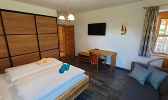 A modern room with a double bed and a cozy sofa. There is a table, a television, and large windows that let in plenty of light.