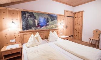 A cozy room with wooden walls and two beds. A beautiful landscape painting of the Alps hangs on the wall.