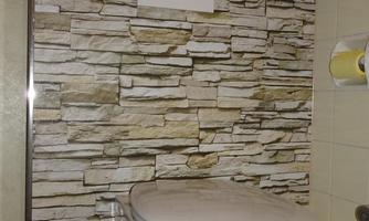 A modern bathroom with a toilet in front of a stone wall. Various toiletries and a toilet paper holder are located on the wall.