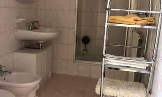 A modern bathroom with a shower, sink, and toilet. A shelf for storing towels and toiletries is available.