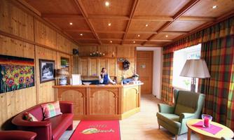 The reception area of a hotel with wooden paneling and cozy furniture. A receptionist stands at the reception desk, while colorful curtains complement the room.